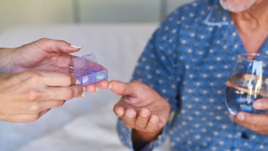 A person giving tablets to a sick senior patient