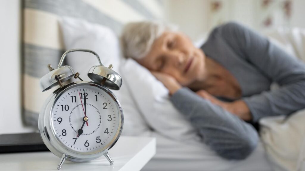 Alarm clock on a bedside table with a elderly woman sleeping