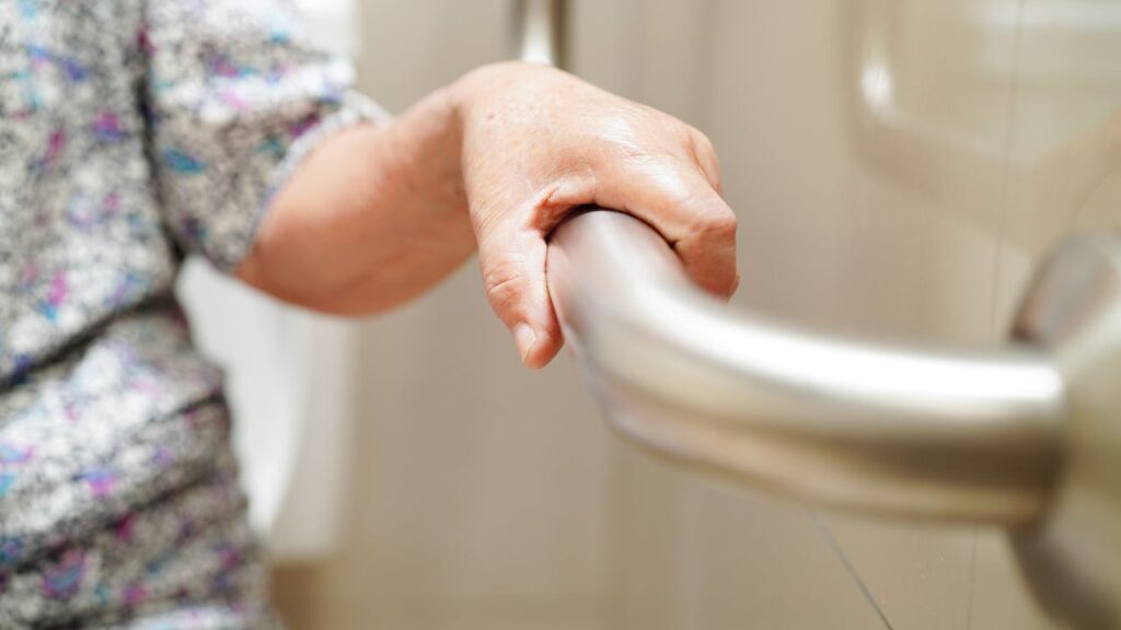 Elderly woman using toilet support rail in bathroom
