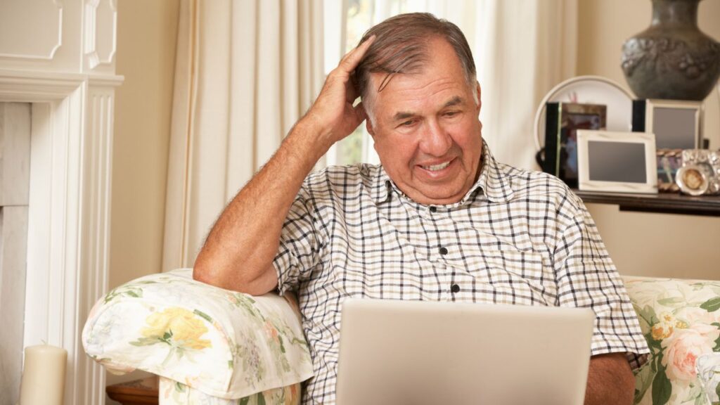 Frustrated senior man sitting on sofa using laptop