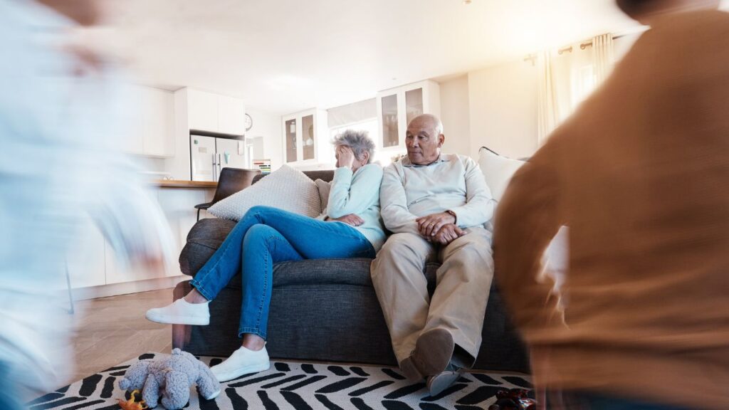 Senior couple sitting on couch looking stressed from the children running