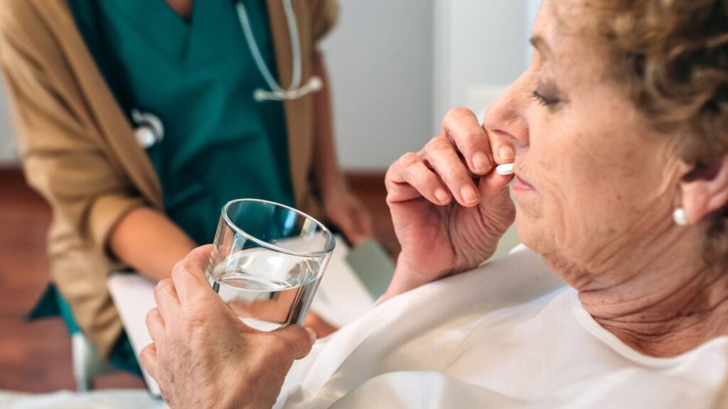 Senior patient taking a pill next to her female doctor