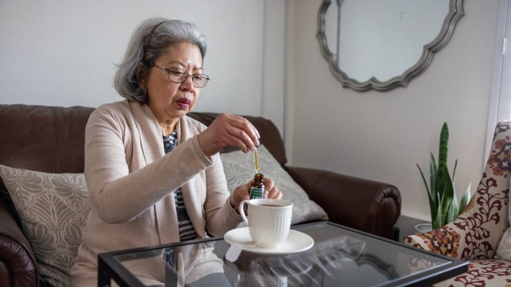 Senior woman using CBD oil in tea at home